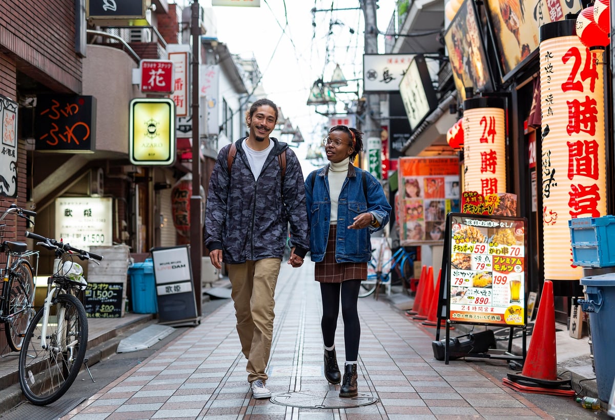 Two smiling people holding hands and walking down a small side street in Tokyo, Japan.