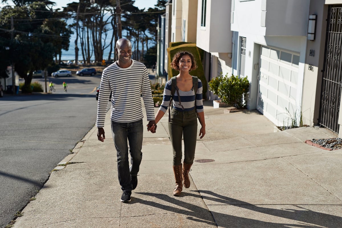 Two smiling people holding hands while walking up a hilly neighborhood street.