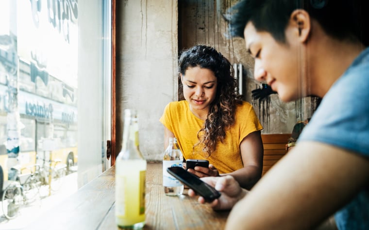 Deux personnes assises à une table près d'une fenêtre dans un restaurant et regardant leurs téléphones portables.