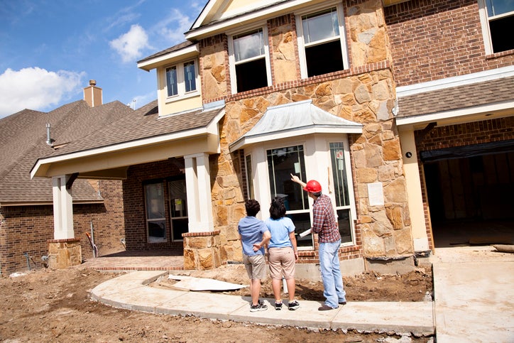 Two women speaking with the builder in front of a partially constructed home.