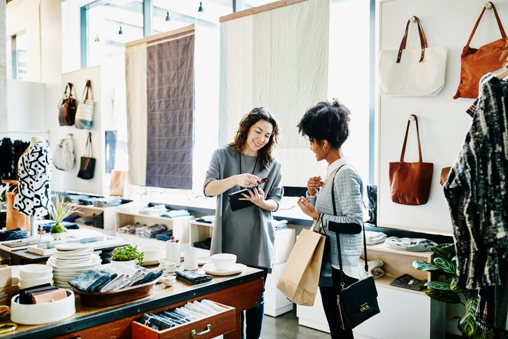 A woman swiping another woman's credit card in a payment reader while standing in a local clothing store.