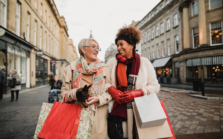 Two women walking down a street arm in arm carrying shopping bags.