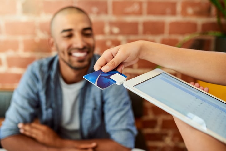 A person looking on as a waiter swipes a credit card in a payment tablet.