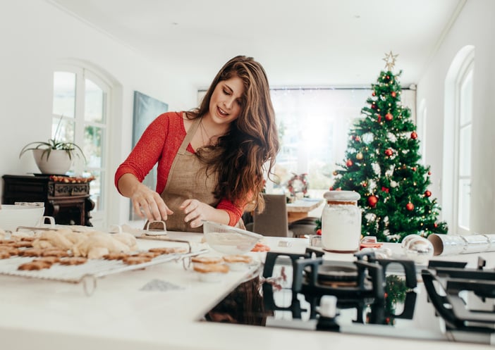 A woman baking cookies in the kitchen with a Christmas tree in the background.