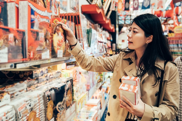 A woman browsing the shelves of a store and picking out boxes of holiday sweets.