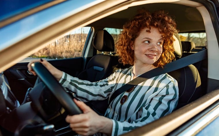 A smiling woman sitting in the driver's seat of a car.