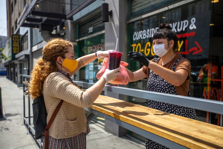 A woman being handed her takeout order from an employee outside a restaurant.