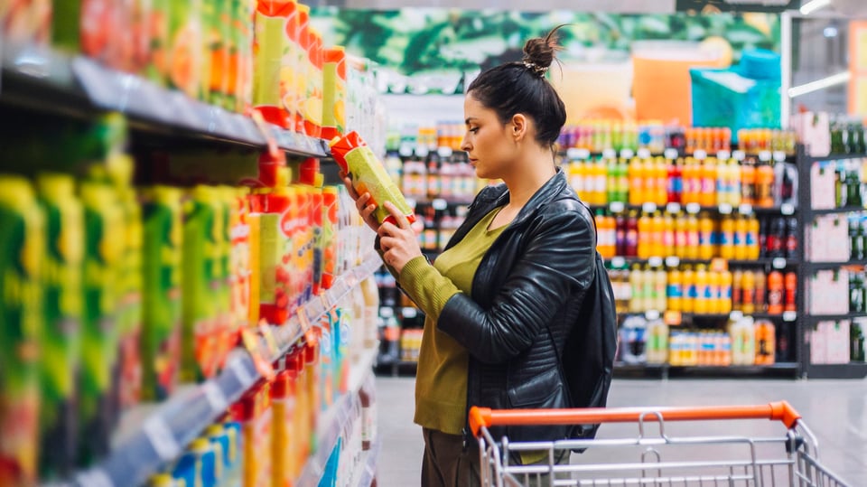 Женщина, сравнивая цены на предмет во время покупки в продуктовом магазине