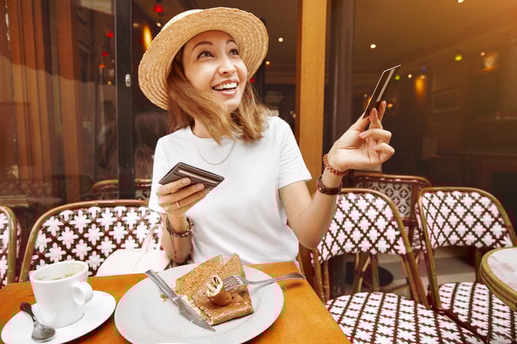 A smiling woman handing her credit card for payment while seated at an outdoor cafe table.