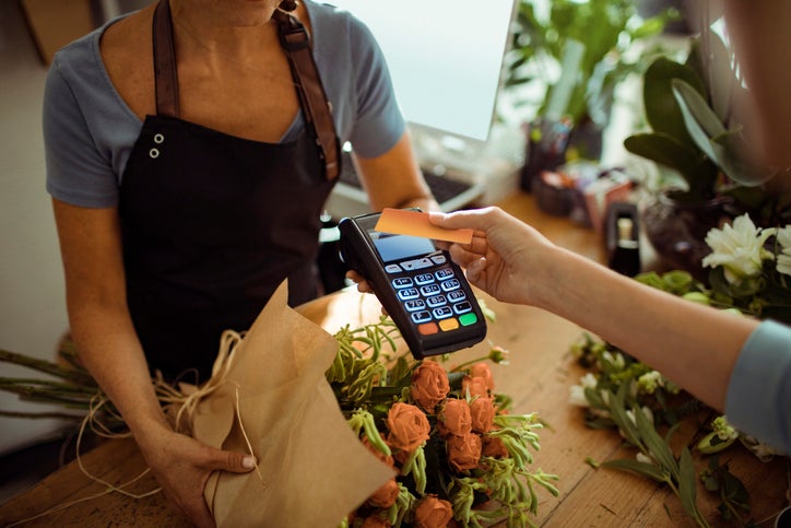 A woman tapping her credit card on a payment reader being held out by a florist in a flower shop.