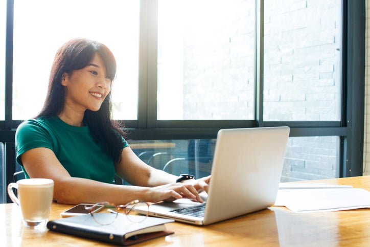 A smiling woman typing on her laptop while sitting in a cafe.