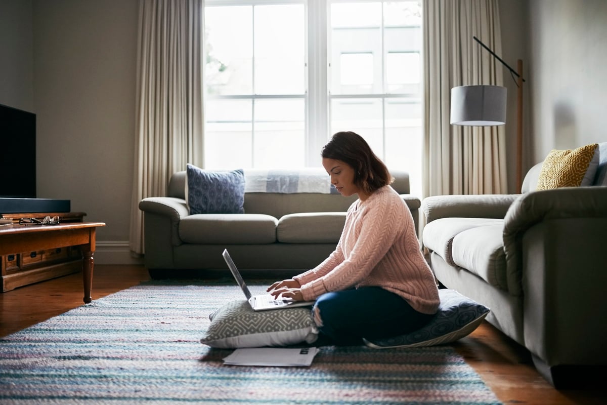 Young woman working from home on a laptop sitting on the floor in the living room.
