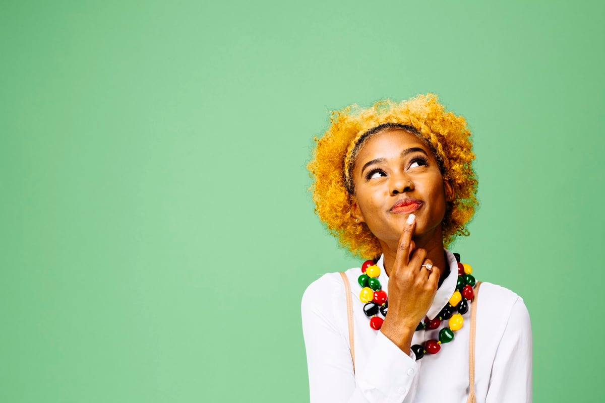 A woman standing in front of the green thinking about her decision with her finger on her chin.