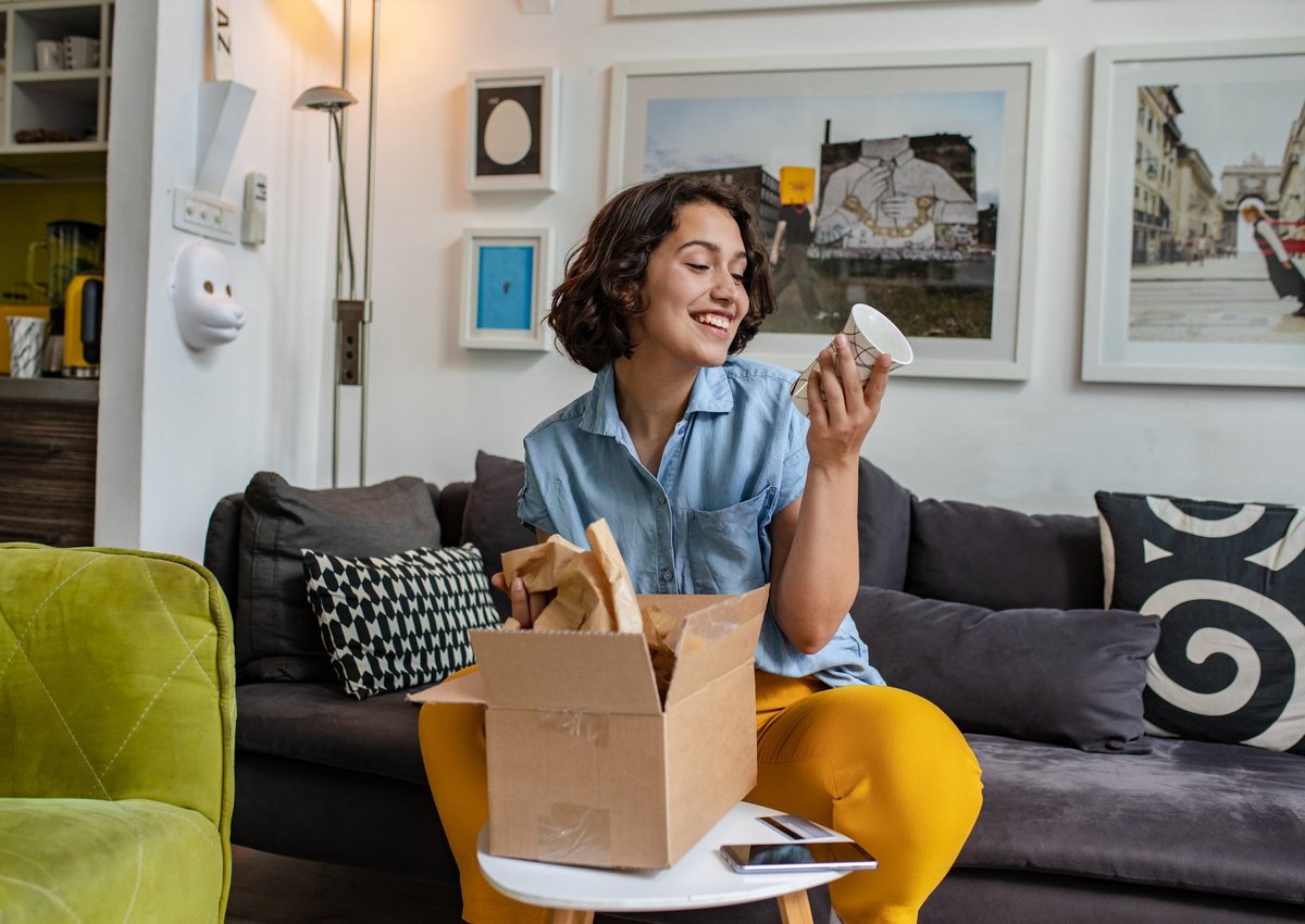 Smiling woman on couch looks at a mug she's getting out of a box