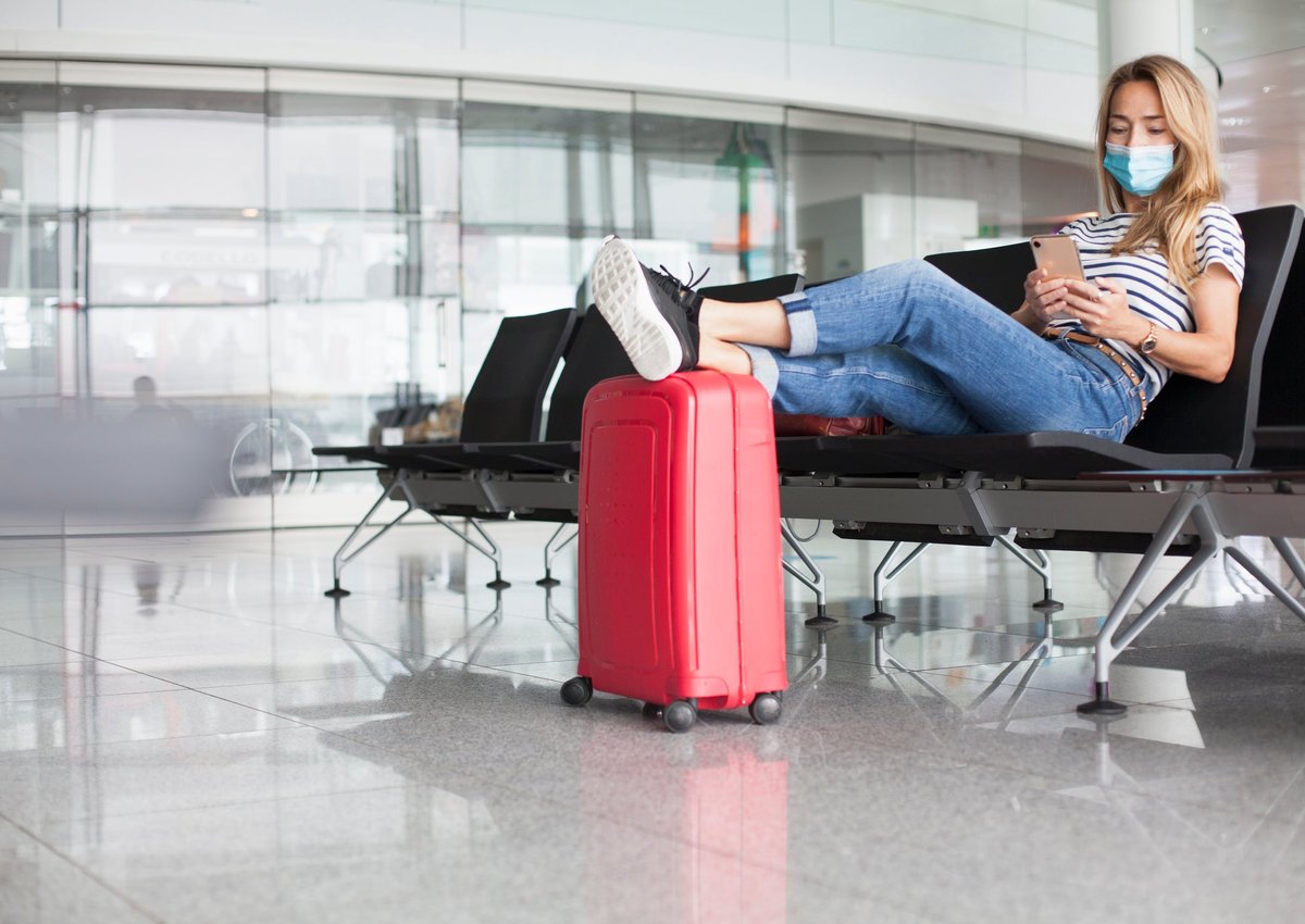 A woman wearing a mask sits and waits at an empty departure gate.