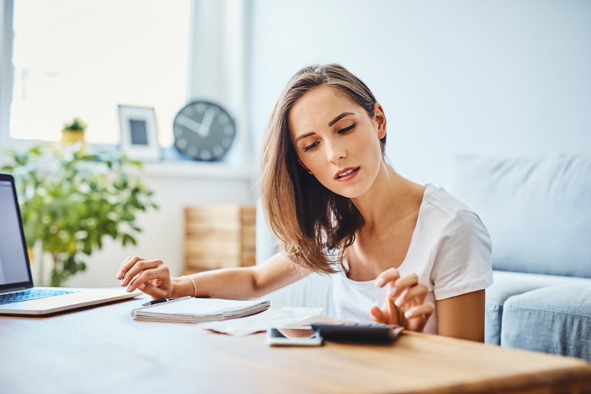 Woman sitting in living room with calculator, notebook and laptop on coffee table.