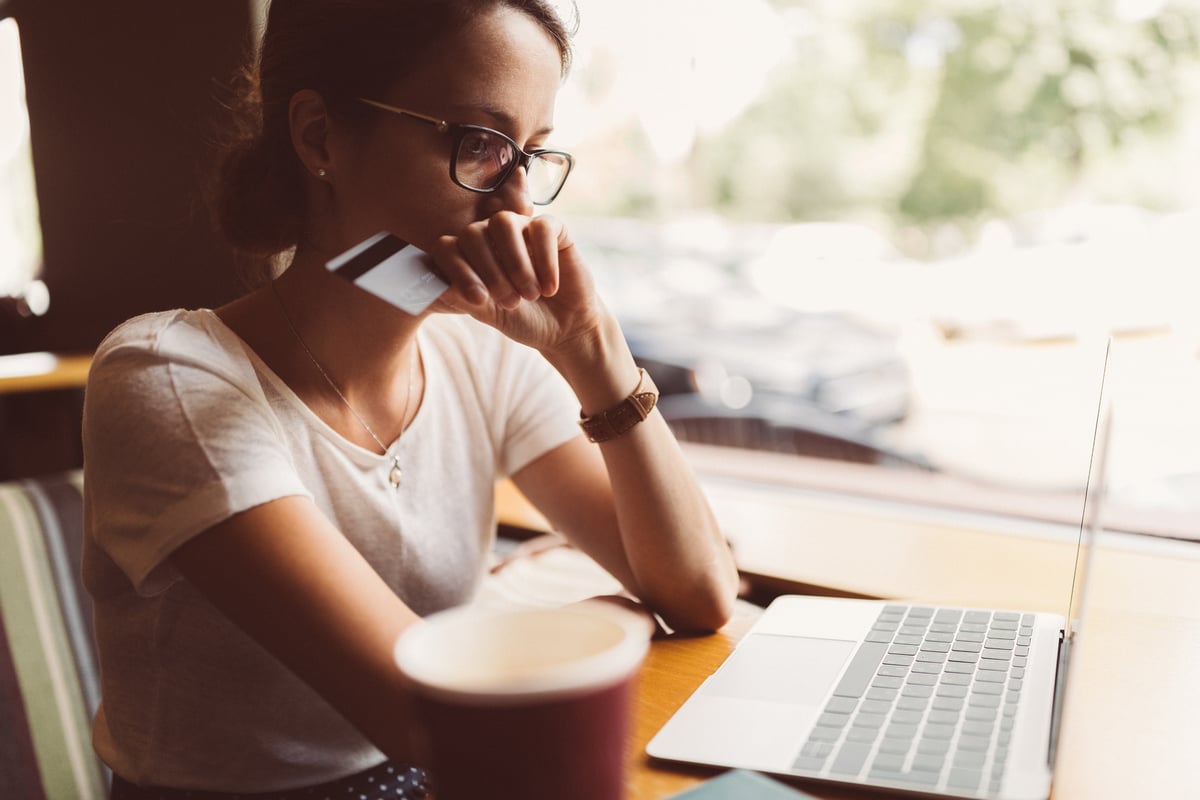 A woman sitting in front of her laptop holding a credit card and looking worried.