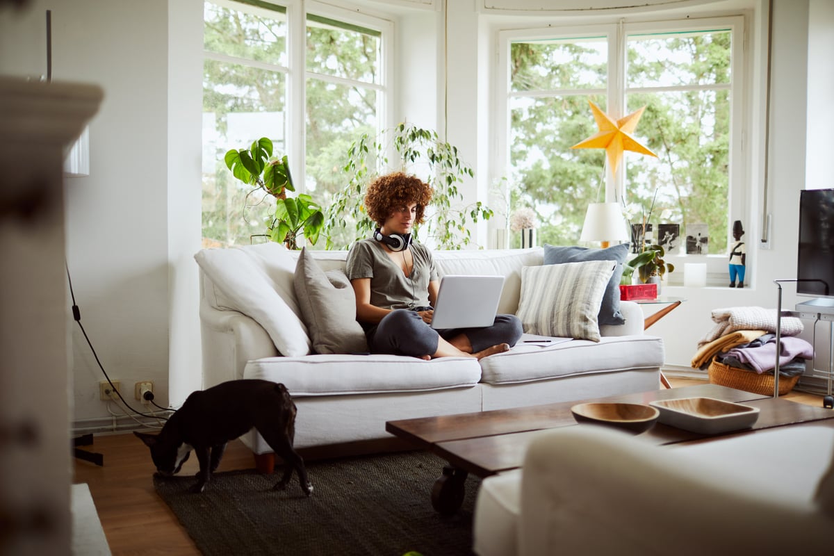 A woman sitting cross-legged on the sofa working on her laptop.