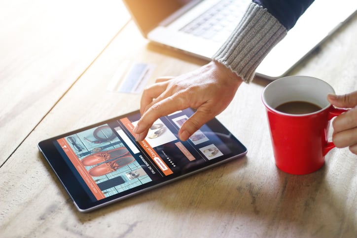 A woman's hand hovering over a tablet open to an online shopping window.