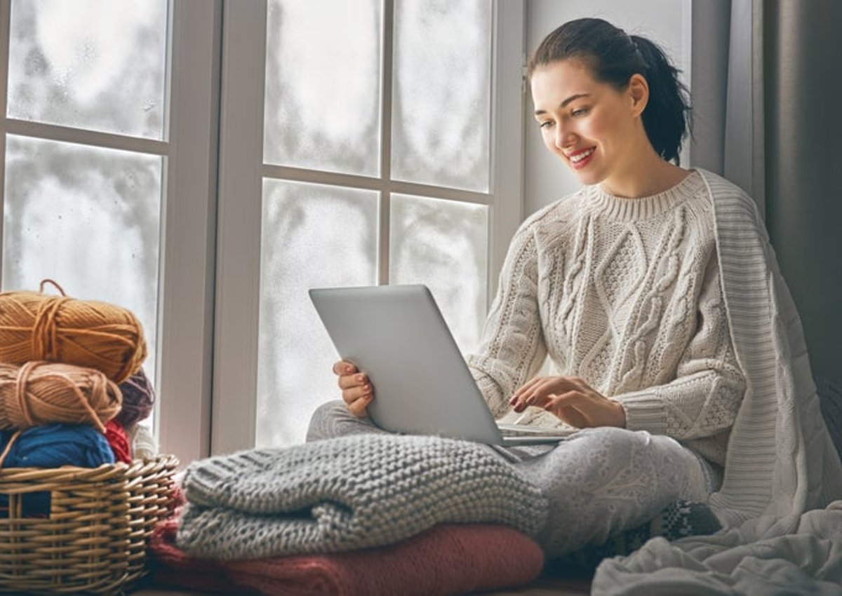 A woman working on her laptop by a window in her home.