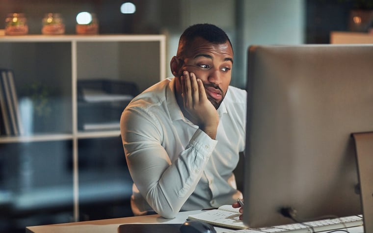 A worried man staring at the computer with his chin in his hand.