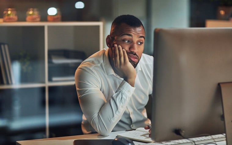 A man holding his chin in his hand and looking at his computer, looking worried.