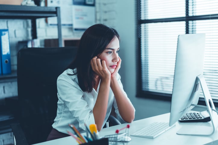 A woman sitting at a desk in front of a computer looking into space with her chin on her hand.