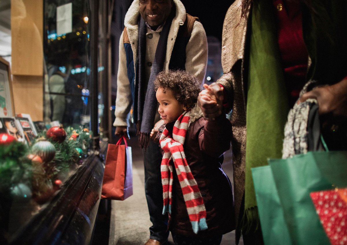 Little child holding hands with parents and looking at holiday window display.