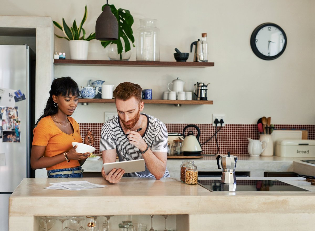 Young couple standing in kitchen and looking on tablet.