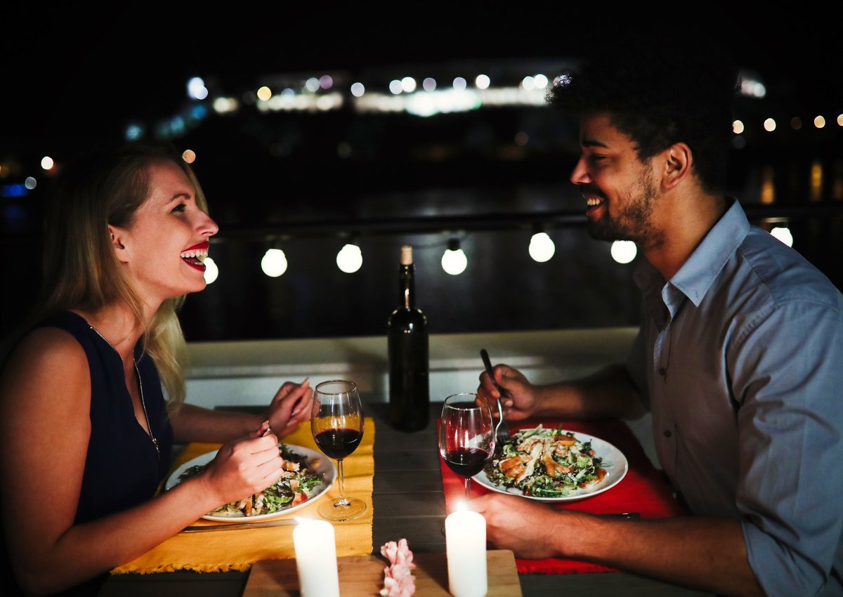 Young man and woman sitting at table eating dinner and laughing.