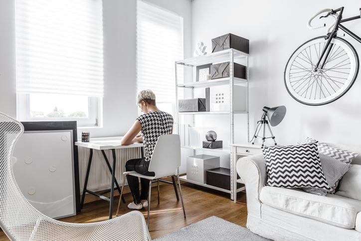 A young woman working at a small desk in the living room of her apartment.