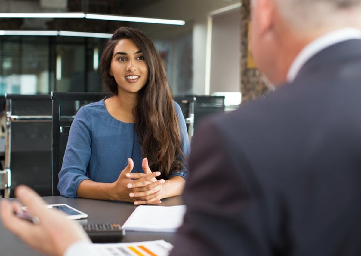 A young woman sits across the table from a man for a job interview in an office.