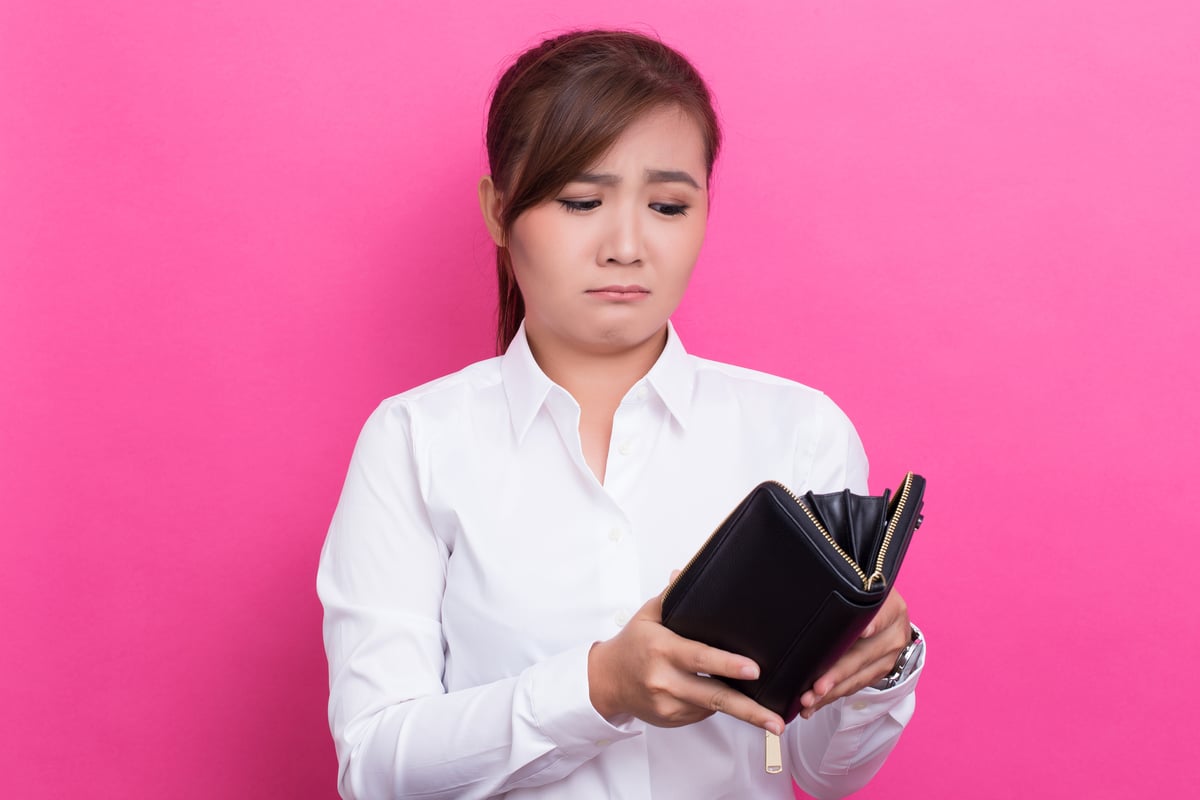 young woman with no money looking into her empty wallet.