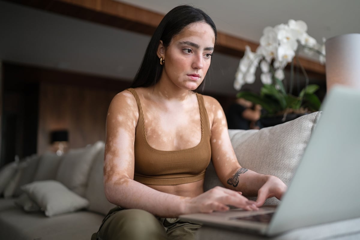 A young woman sits on her couch, reading the days news on her computer.