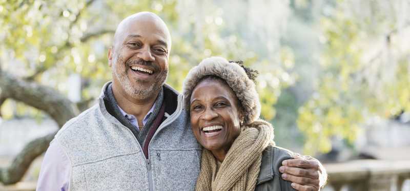 Two people smiling and standing arm in arm outside.