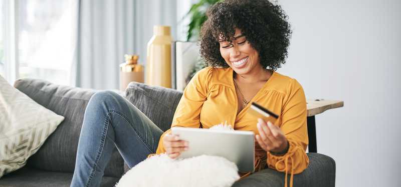 Person holding credit card while looking at tablet and sitting on couch.
