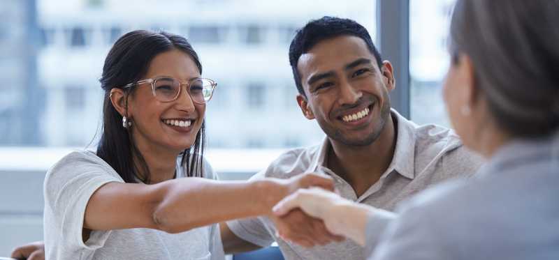 Two people shake hands with consultant over paperwork in an office.