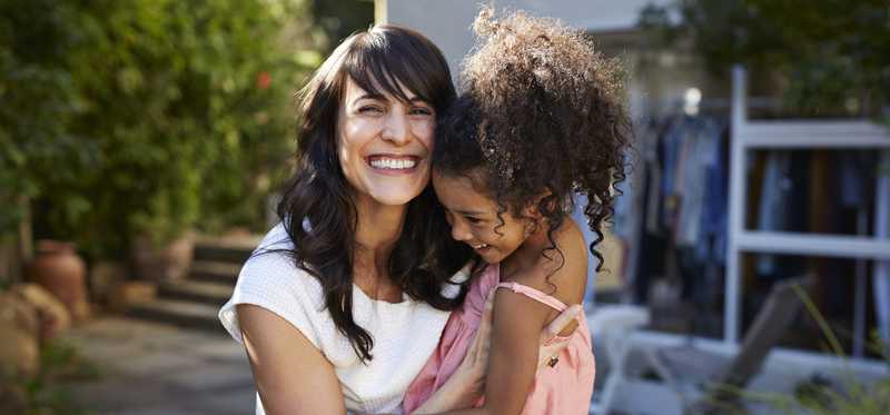 Happy adult holding smiling child on an outdoor patio.