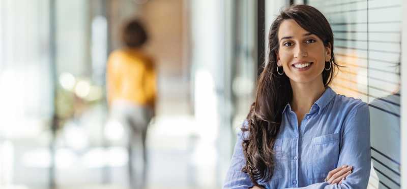 Person smiling and leaning against window in office.