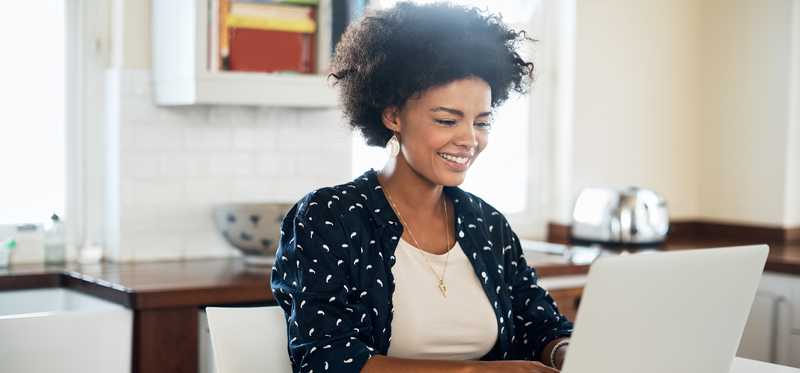 Person smiling while using laptop in a kitchen.