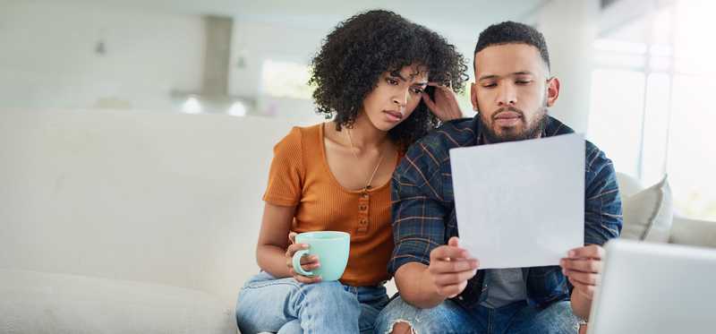 Two people sitting on couch and looking worriedly at document.