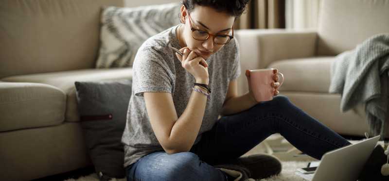 Person sitting on living room floor and looking thoughtfully at laptop.