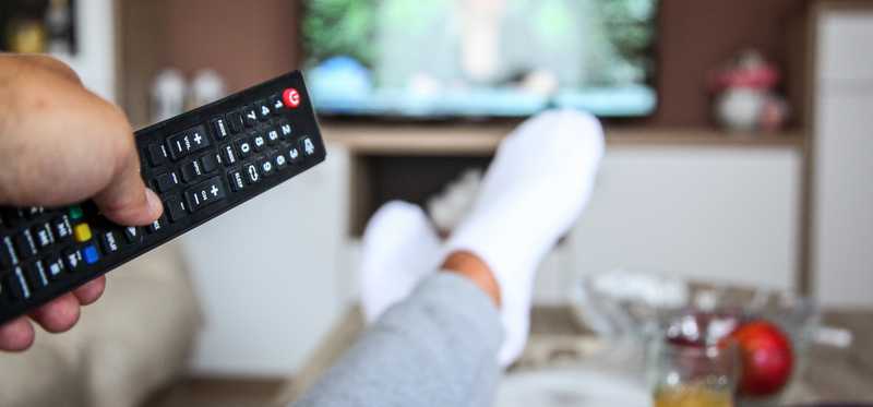 Man with his feet up holding remote aimed at TV.