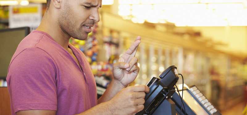 A guy crosses his fingers as he swipes his credit card.