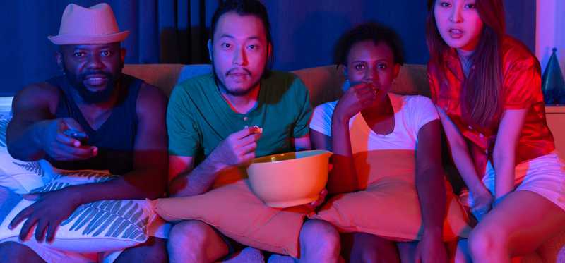 A group of friends watching tv in dimly lit room.
