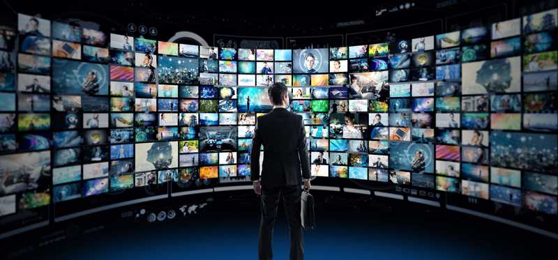 Man in front of wraparound screen with dozens of different images.