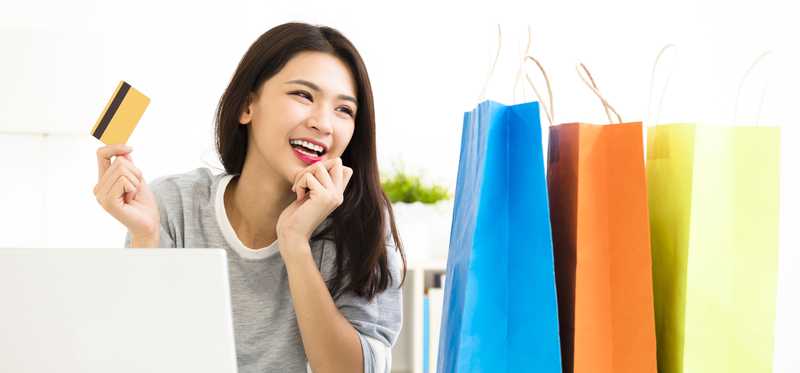 Woman on laptop smiles holding credit card near shopping bags.