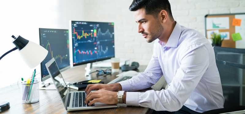 Person looking at stock charts on multiple screens.