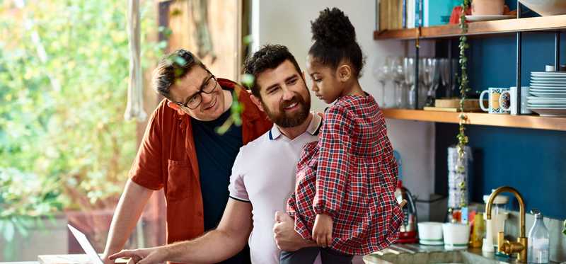 Two adults and a child with a laptop in a kitchen.