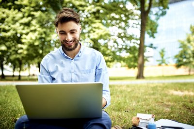 Smiling adult sits outside in the park with laptop.